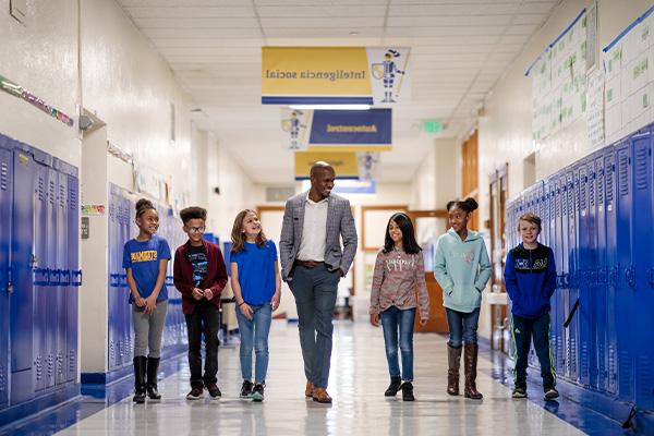 Elementary-school students walking alongside a teacher in the school's hallway.